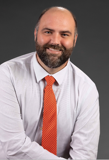 Photo of smiling man with white shirt and orange tie with navy polka-dots