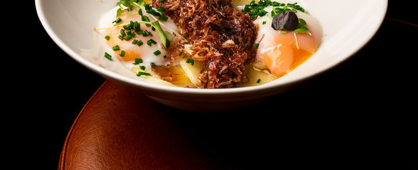 Plato gourmet con huevos pochados, trufa y cebollino sobre fondo oscuro, fotografía gastronómica profesional en Barcelona para restaurante.