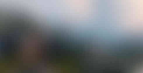 Two players in orange suits stand on a rocky cliff overlooking a massive industrial base. Glowing blue power lines connect various high-tech buildings and towers across the valley.