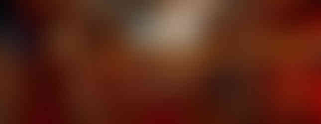 A wide shot of a grand, two-story library with high ceilings, many bookshelves, a spiral staircase, a chandelier, and a few characters relaxing in armchairs.