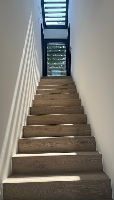 Holztreppe mit Lichtstreifen durch Lamellen und Oberlicht