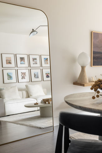 Interior of a small living room designed with warm minimal and organic elements, featuring a sheepskin lounge chair paired with a microcement coffee table with an earthy, stone-like finish. A travertine side table framed in white oak with leather and brass detailing sits nearby, alongside a hand-knotted wool rug, white oak floating shelves, and soft layered lighting. A large terracotta planter with a minimal tree adds an organic focal point.
Living space detail showing layered materials including a microcement coffee table, wool rug, and soft textile accents. A sheepskin lounge chair introduces contrast and softness, while natural light enhances the warm, sun-washed tones of the stone and wood surfaces.
Close up view of a travertine side table with white oak framing, leather wrapping, and antique brass hardware. The piece sits against a softly styled living area, emphasizing texture, craftsmanship, and tactile materials.