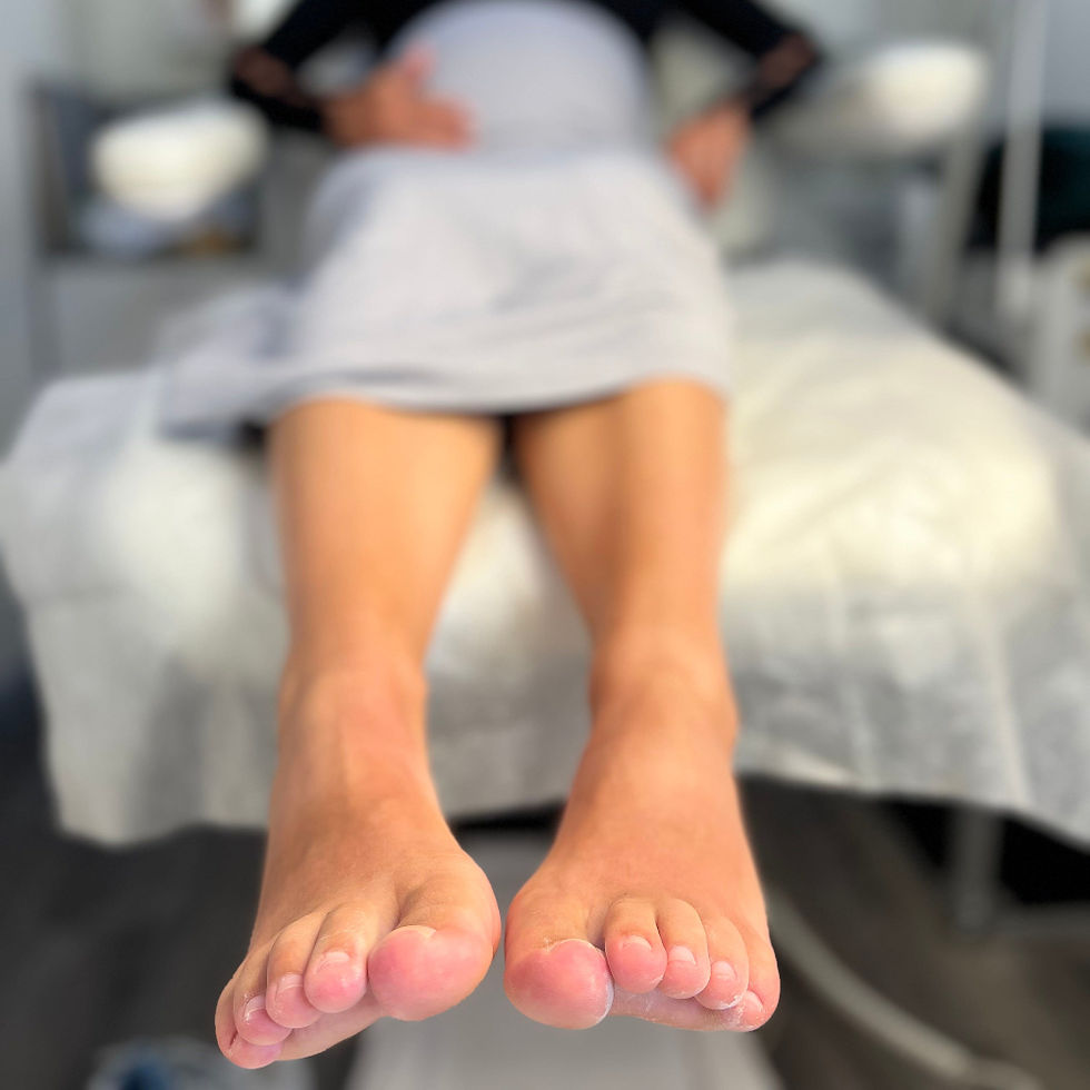Close-up view of two bare feet held slightly above a medical exam chair, with toes facing forward. The skin around several toes appears pink and slightly irritated, with some dry or peeling areas visible. The background is softly blurred, suggesting a clinical or treatment setting.