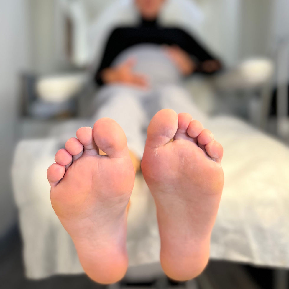 Close-up view of two bare feet held slightly above a medical exam chair, with toes facing forward. The skin around several toes appears pink and slightly irritated, with some dry or peeling areas visible. The background is softly blurred, suggesting a clinical or treatment setting.