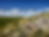 A wide, open prairie landscape under a blue sky with scattered clouds, showing tall grasses and rocky outcrops in Grasslands National Park.