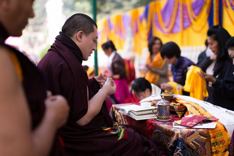 An attendee arranges folded ceremonial cloth and offerings on the table — Bodh Gaya, Bihar, India — December 2014 — Monlam 2014 - Day 7 - Dreams, Goodbyes and Memories — photograph by Tokpa Korlo