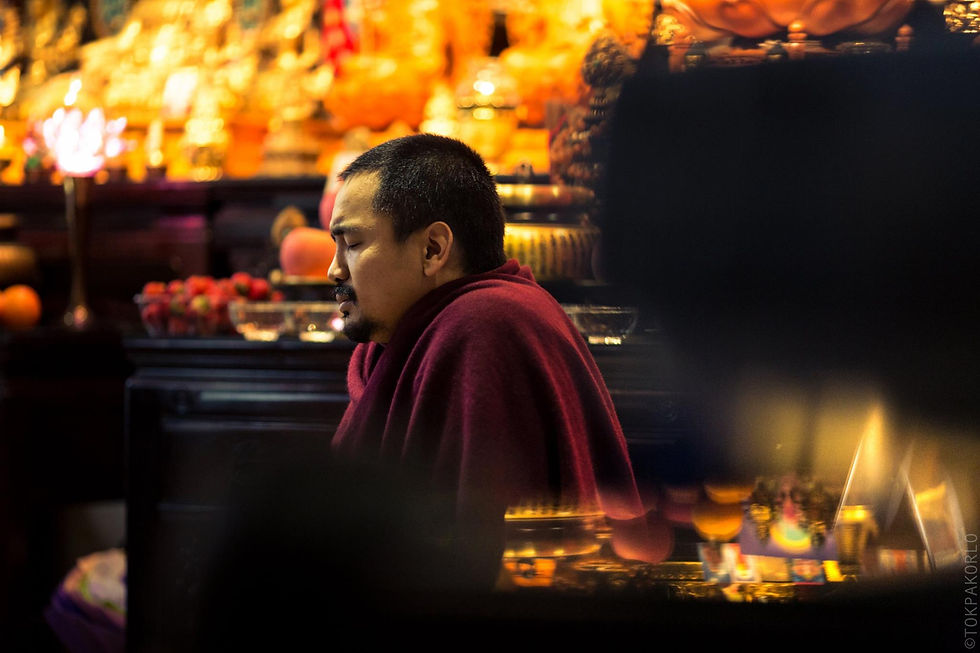 A figure in dark robes sits in profile within a dim interior lit by warm shrine details — Qingdao, Shandong, China — March 9, 2016 — Qingdao - Shadow Dharma — photograph by Tokpa Korlo