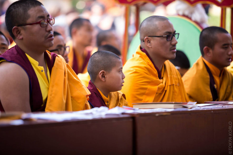 A child and three adults in yellow and maroon robes sit behind a wooden prayer table — Bodh Gaya, Bihar, India — December 2014 — Monlam 2014 - Day 2 - The Golden Sun — photograph by Tokpa Korlo