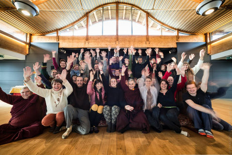 A large group raises arms together for a joyful closing portrait — Dhagpo Kagyu Ling, Dordogne, France — February 2015 — A Tara Morning — photograph by Tokpa Korlo