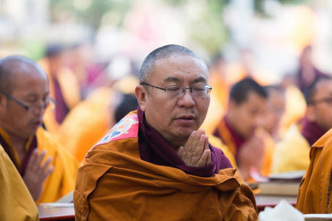 An older attendee in yellow robes watches quietly from the gathering — Bodh Gaya, Bihar, India — December 2014 — Monlam 2014 - Day 6 - Of Light and Fire — photograph by Tokpa Korlo
