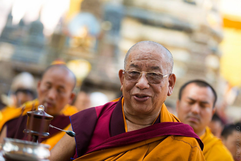 An older attendee in glasses and yellow and maroon robes holds a prayer wheel outdoors — Bodh Gaya, Bihar, India — December 2014 — Monlam 2014 - Day 3 - Offerings of Warmth — photograph by Tokpa Korlo