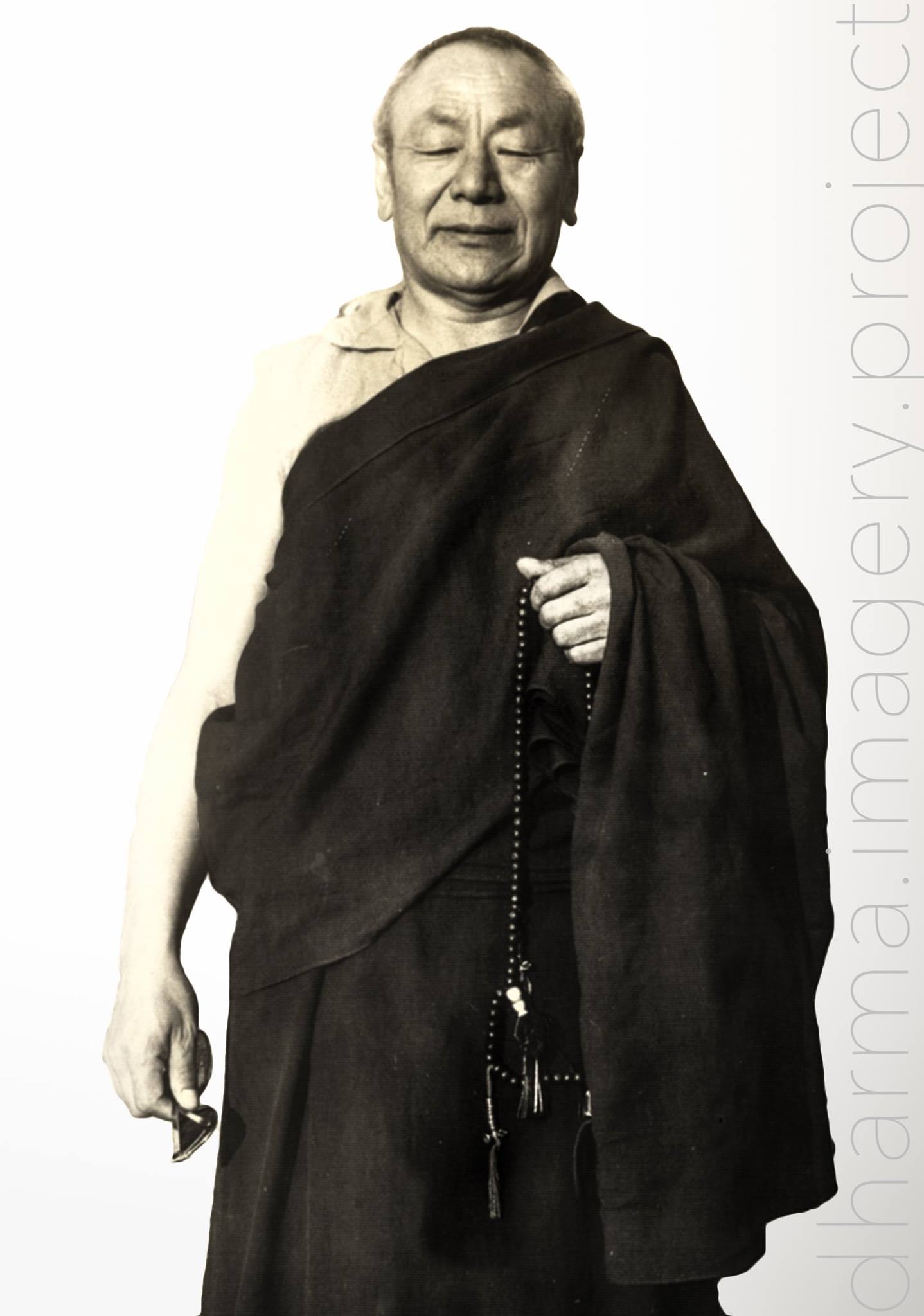 Monochrome archival portrait of a standing robed figure holding prayer beads — original photograph by an unidentified photographer; remastered by Tokpa Korlo