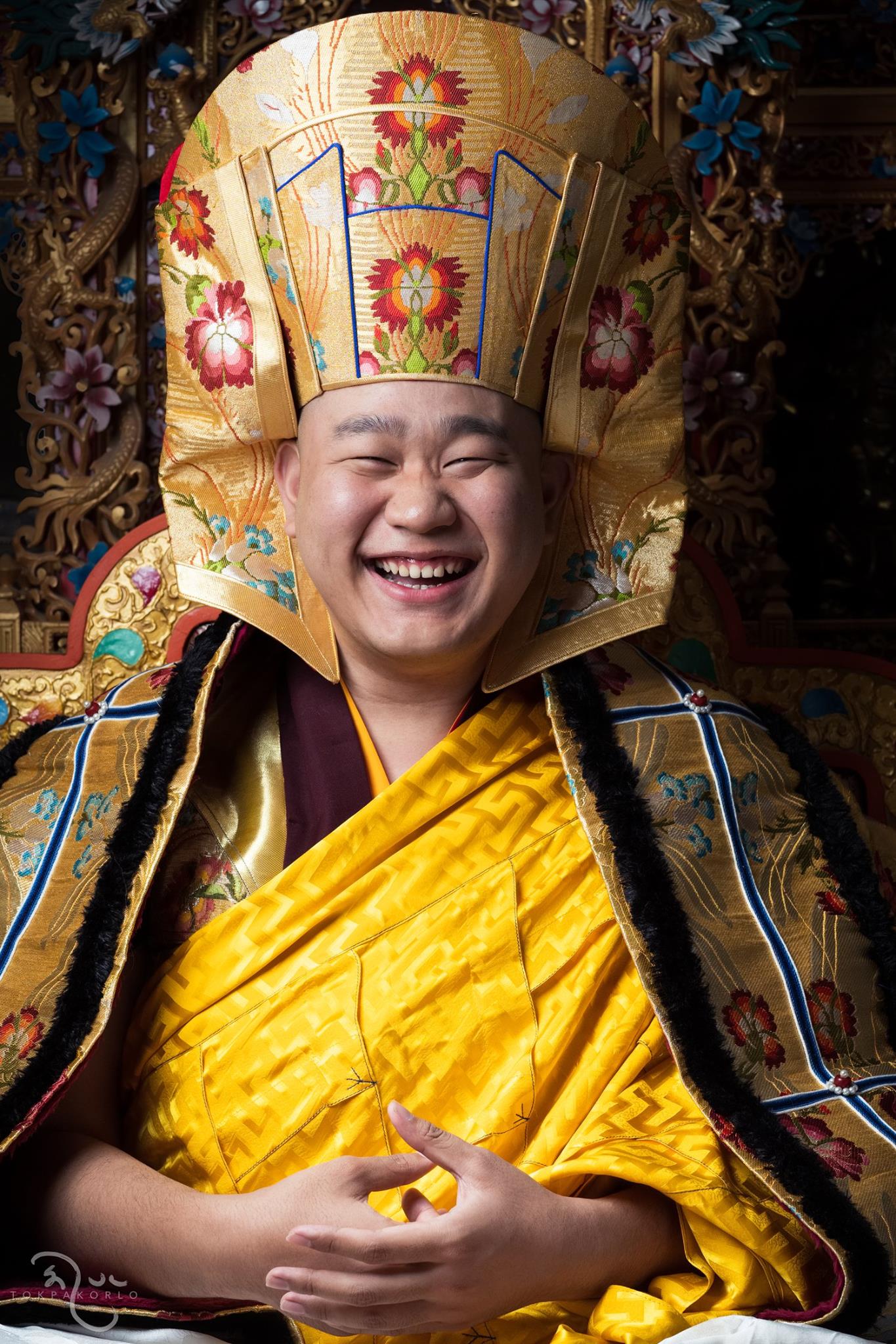 A smiling figure wears richly patterned ceremonial robes and a tall embroidered hat — The Dharma Studio — Oct 31, 2018 — The Dharma Studio - Jamgon Kontrul Rinpoche — photograph by Tokpa Korlo
