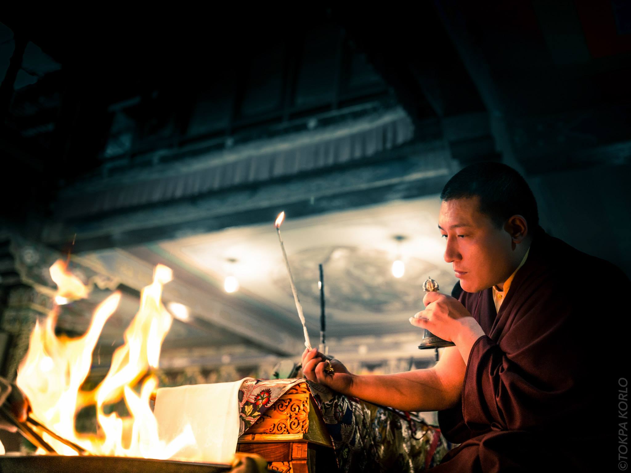 A figure works beside a small illuminated shrine in a nearly dark interior — Sep 15, 2015 — The Beauty Of Darkness — photograph by Tokpa Korlo