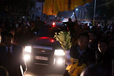 A vehicle moves slowly through the nighttime crowd beneath the yellow canopy — Bodh Gaya, Bihar, India — December 2014 — Monlam 2014 - Day 4 - Karmapa Arrives — photograph by Tokpa Korlo