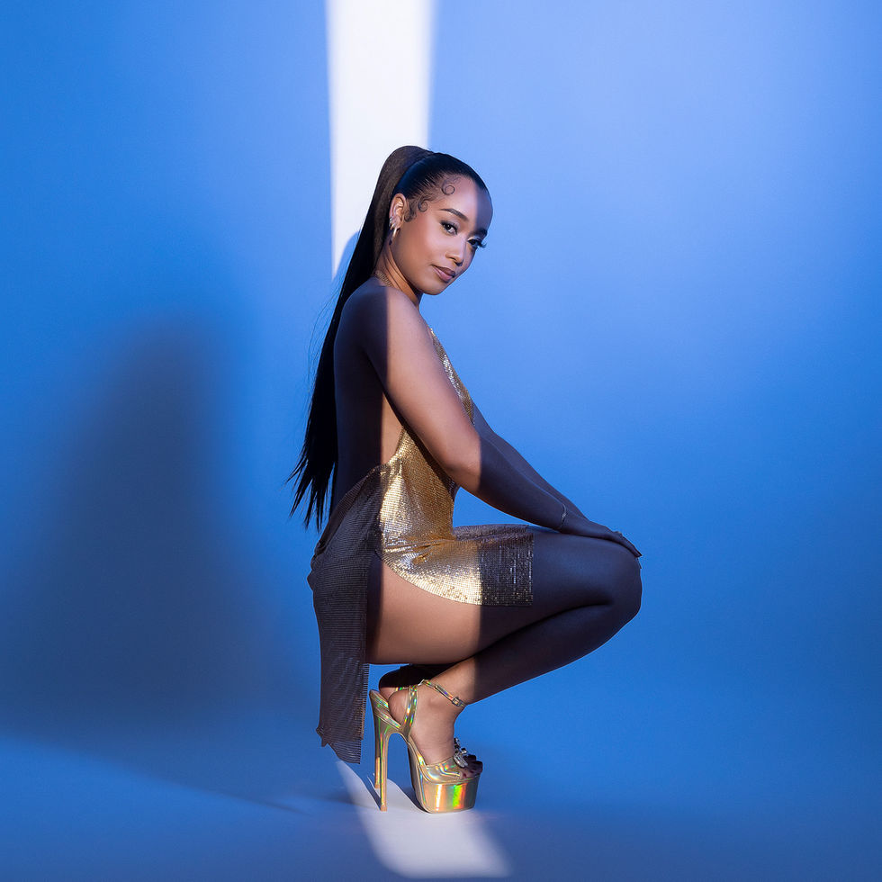 Woman posing in gold outfit, blue background.