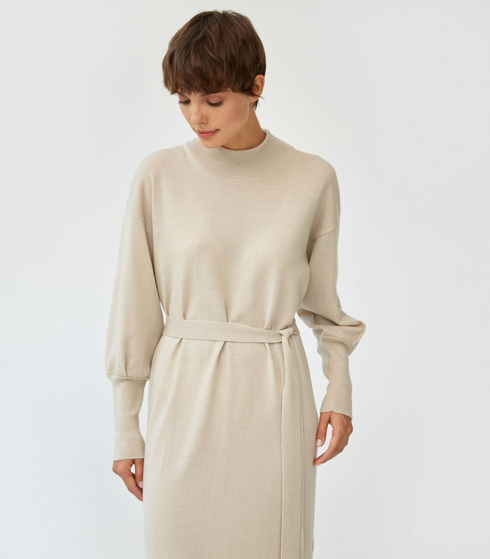 Fashion lookbook photography by Kumar Piyush — woman wearing cream belted long-sleeve dress against neutral white background