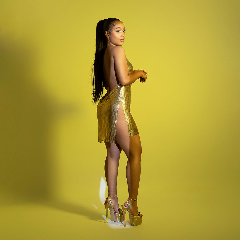 Woman in gold dress and heels, yellow background.