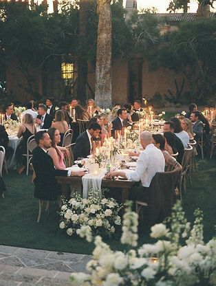 an evening candlelit table with 100 or so guests eating and talking over dinner at sunset
