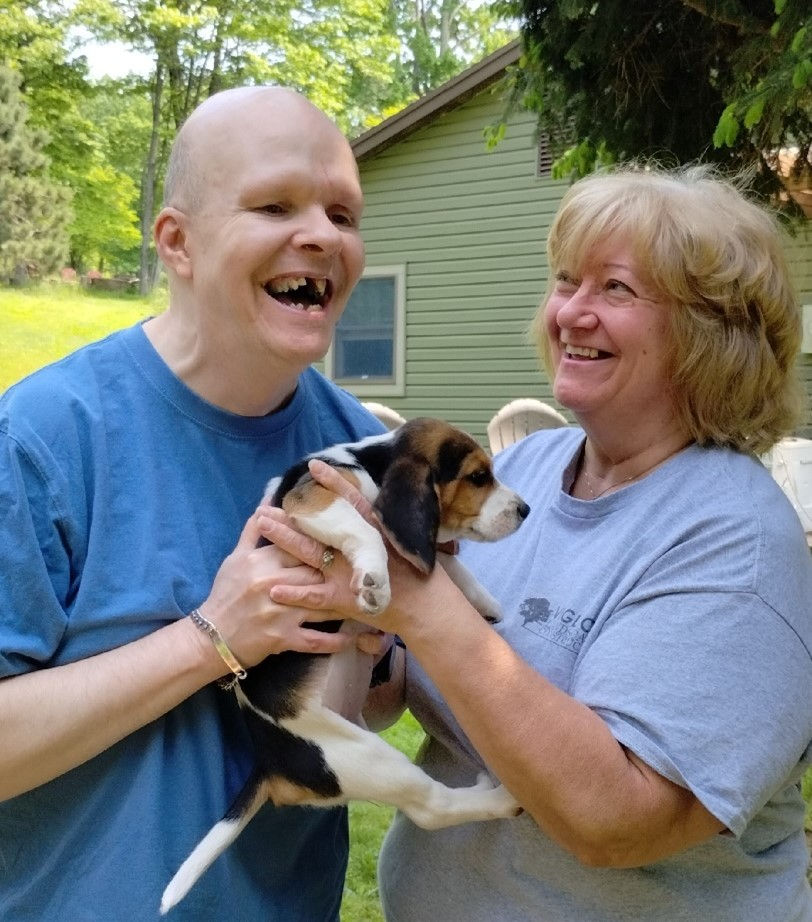 Man and woman smiling while holding a beagle puppy outdoors.