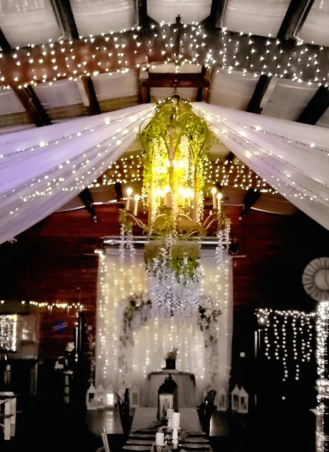 View looking up at the high ceiling of the Rayshell Ranch barn decorated with twinkling string lights and a chandelier.
