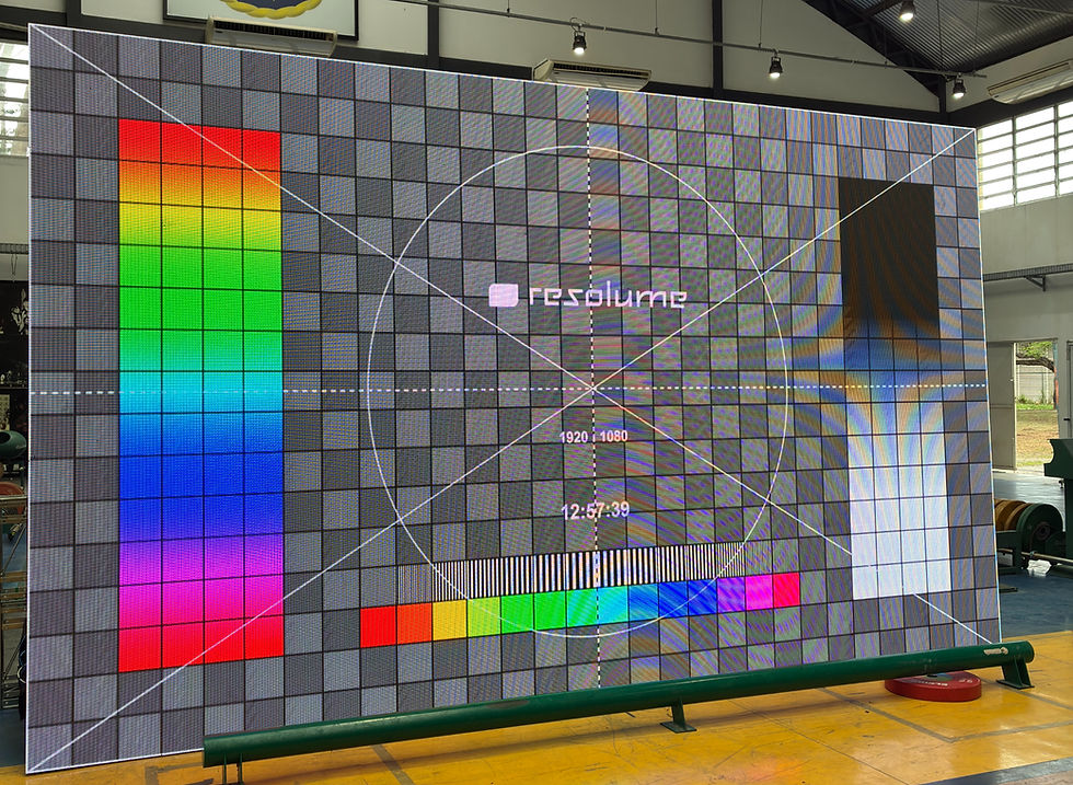 Painel LED gigante em teste de imagem com padrão colorido, grade cinza, texto resolume e 1920x1080 em galpão industrial.