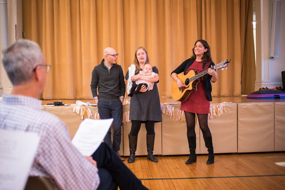 Cantor Stein playing guitar and singing with parents and their baby at a Jewish Baby Naming ceremony in New York City, New York