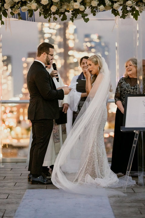 a bride wiping her tears as her groom reads his vows at their co-officiated wedding in New York City, New York