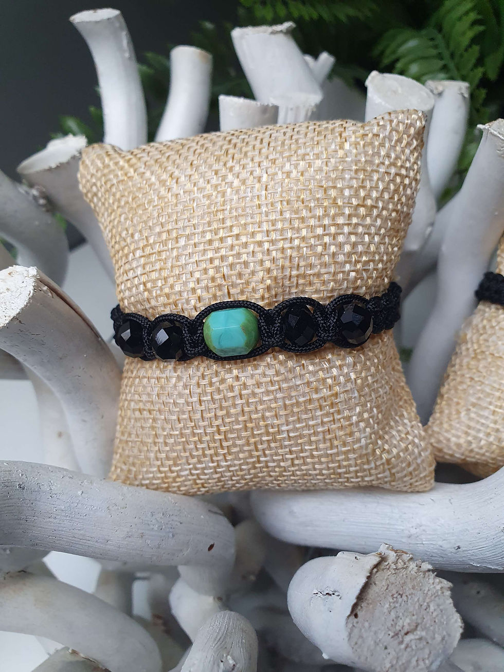 Miniature : Bracelet noir avec une perle turquoise sur un présentoir en toile de jute.