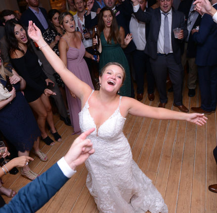 Bride with arms out wide in pure joy and celebration on the dance floor at Bournedale Function Facility in Bourne MA while guests look on surrounding her