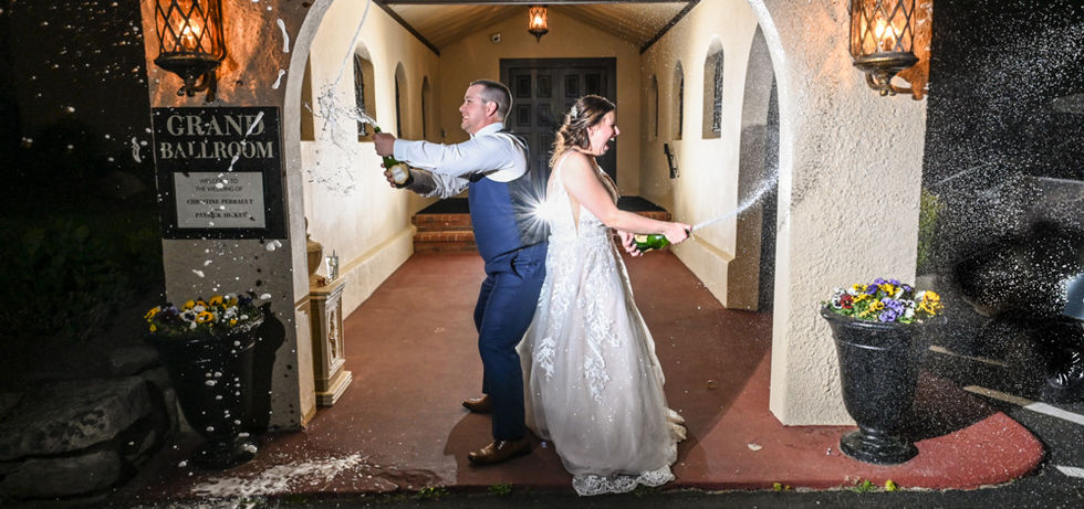 Night shot of bride and groom lit by two flashes as they shake and spray champagne outside the Grand Ballroom at The Villa in East Bridgewater MA