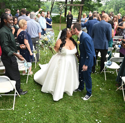 Bride and groom kiss at the center of the aisle as guests throw confetti in celebration of their wedding at Loon Pond Lodge in Lakeville MA