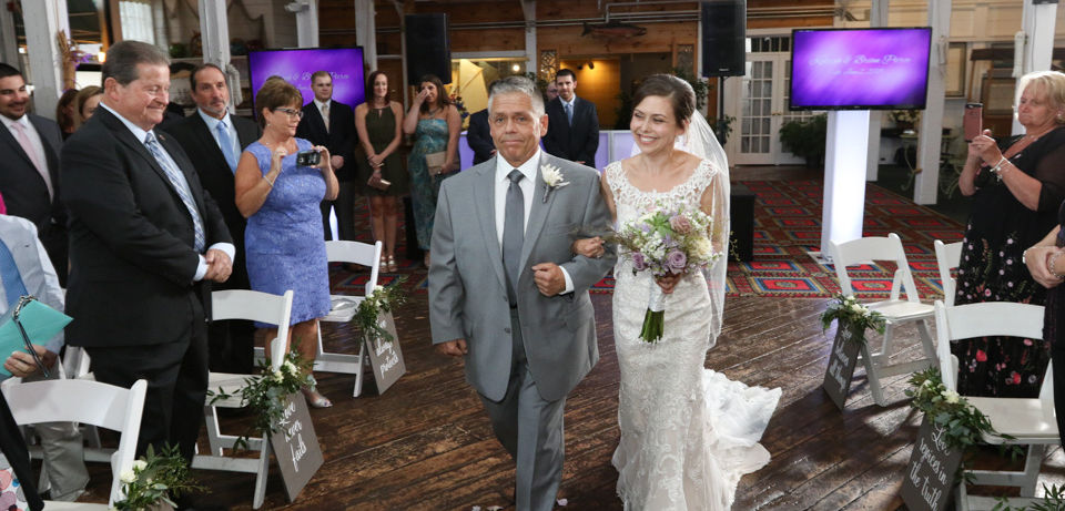 Bride is walking down the aisle on dads arm with guests seated on either side at Jones River Trading Post in Kingston MA