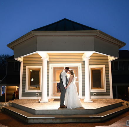 Couple standing at the entrance to Camp Bournedale Function Facility in Bourne MA at night with rain around them.