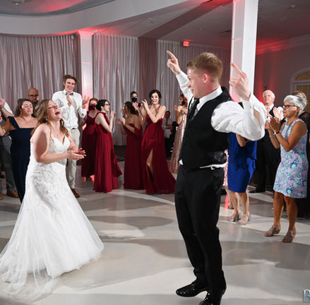 Bride laughing while groom does goofy dance move surrounded my guests on their dance floor at their wedding at Avenir in Walpole MA