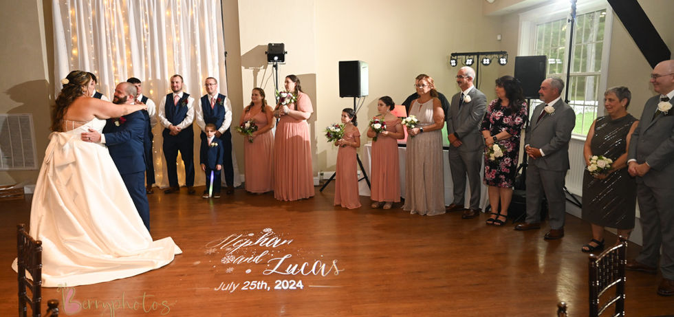 The first dance for this wedding couple on the dance floor at Loon Pond in Lakeville MA with guests and family lining the side and their names projected onto the wooden floor with a projector at Loon Pond in Lakeville MA