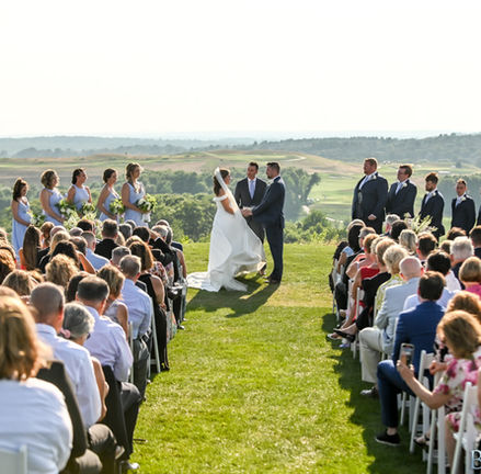 Wide shot of the guests seated watching the bride and groom exchange vows.  The wedding party stands in support on each side.  Behind them are the rolling greens of the golf course blending seamlessly into the Blue Hills in the distance.  It's an elevated plateau giving a sweeping view that's clean and stunning at Granite Links in Quincy, MA