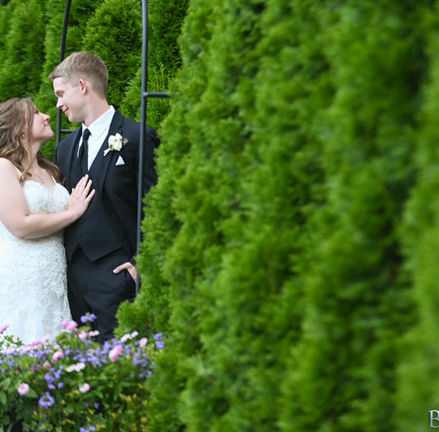 Couple standing amongst spring flowers along row of greenery at Avenir in Walpole MA