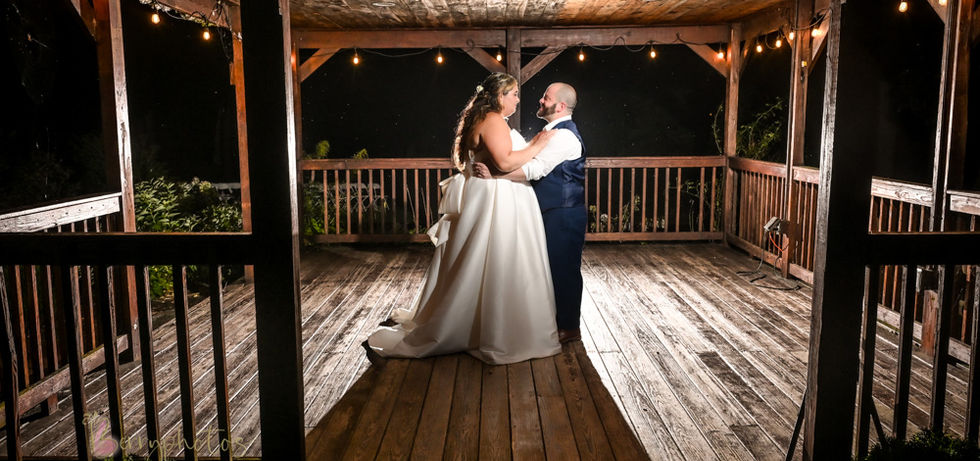 Bride and groom standing inside a large wooden gazebo back lit with flash and just a touch of flash from the front to create something truly amazing and noteworthy at Loon Pond in Lakeville MA