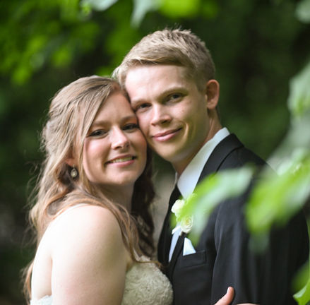 couple looking at camera and smiling surrounded by green leaves in spring pictures at Avenir in Walpole MA