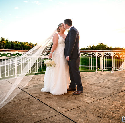 Natural light photography at sunset with bride and groom kissing and the brides vail caught in the wind as the sun sets to the right at Indian Pond in Kingston, MA