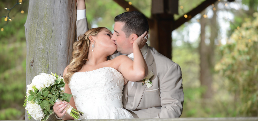 Bride leans back over her shoulder to steal a kiss from the groom on the front porch of Camp Kiwanee in Hanson MA during a quiet moment of their wedding day.