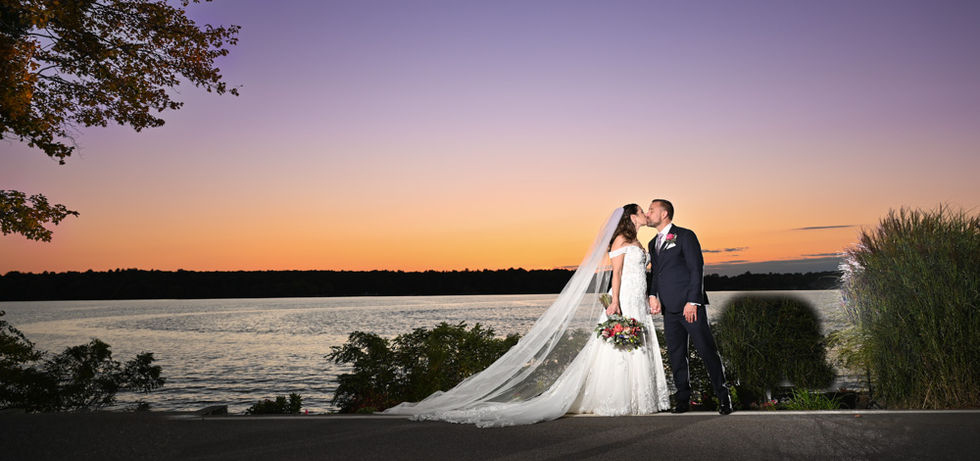 Bride and groom perfectly lit with flash as they stand at the lake with the most amazing unset behind them.  No AI and No Photoshop, just amazing skilled wedding photography.