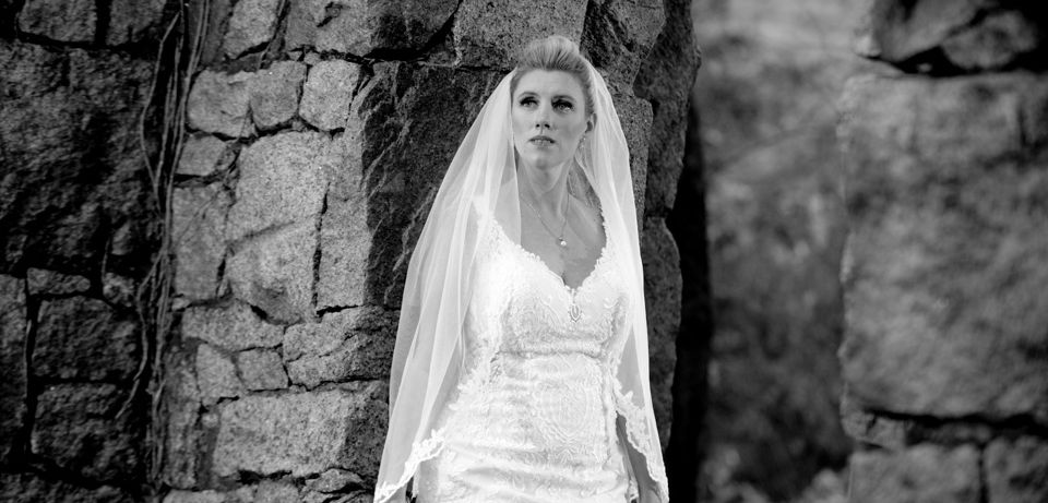 Black and white photo of bride leaning against a rock wall at Granite Links in Quincy, MA