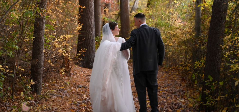 Bride and groom walking away from the camera along a path that cuts through the tall trees and fall foliage along the lake at Camp Kiwanee in Hanson MA