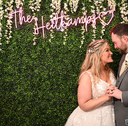 Bride and groom stand in front of a green leaved backdrop at their wedding at Camp Bournedale Function Facility in Bourne MA