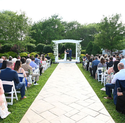 wide shot of the outdoor wedding ceremony area at The Villa in East Bridgewater MA with couple standing at pergola with guests seated watching.