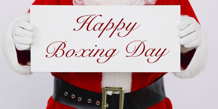 Santa holding a white sign with "Happy Boxing Day" in red script. He wears a red suit with a black belt, creating a festive mood.