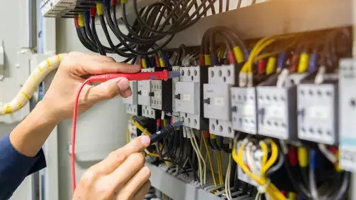 Electrician with multimeter testing electrical panel wires, circuits, and connections. Microfirm Training