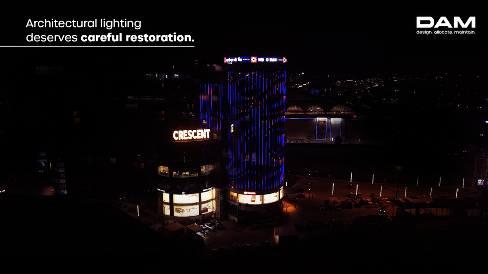 Night view of a commercial building with illuminated architectural facade lighting, featuring the text “Architectural lighting deserves careful restoration” and DAM Solutions branding.
